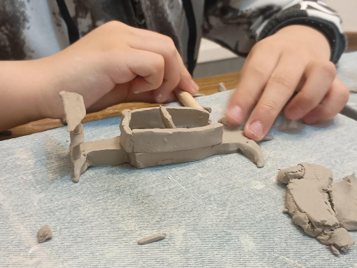 Manos construyendo una pieza de arcilla en la mesa del taller.