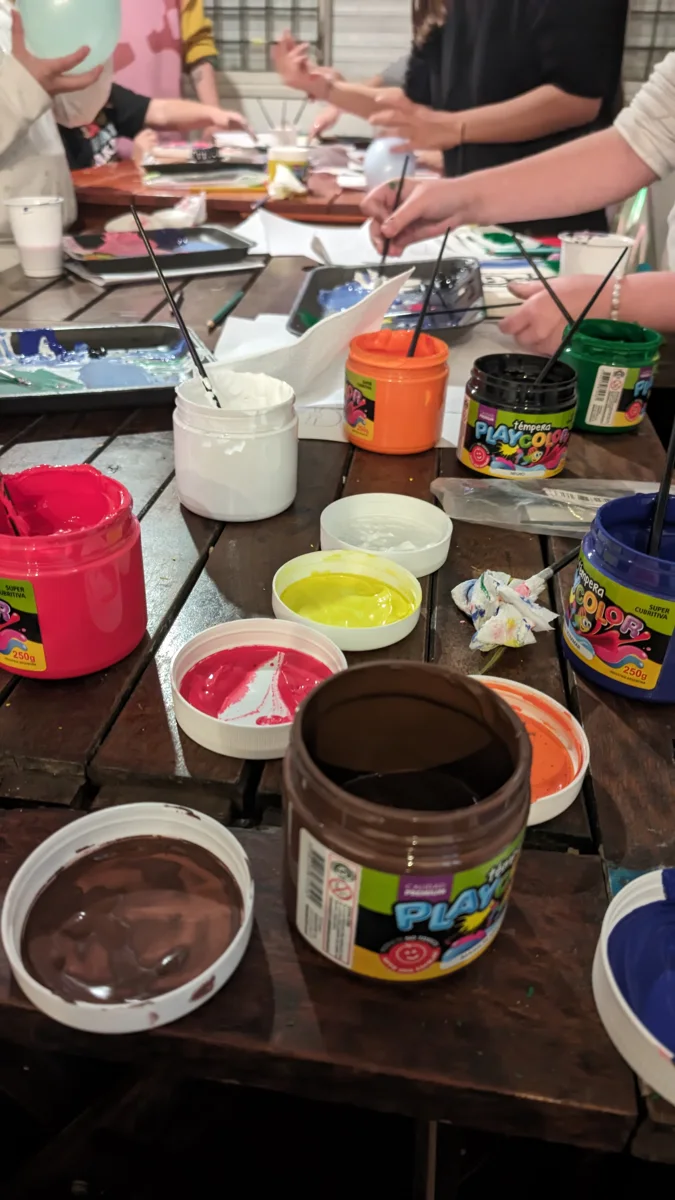 Manos pintando bastidores alrededor de una mesa con pinturas de colores.